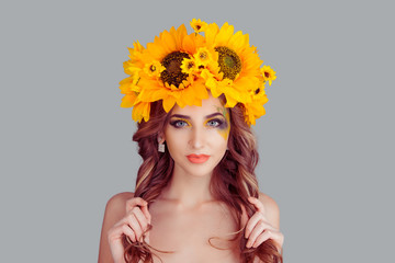 Portrait beautiful young woman wearing floral headband isolated on gray background. Sunflowers wreath of flowers on head looking at camera girl hand holding showing healthy curly hair