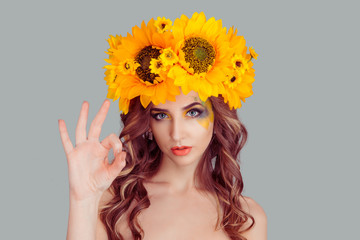 Attractive young adult Woman with floral headband showing ok sign. Expression emotion and feelings concept. Studio shot, isolated on gray background. Fashion girl with crown from sunflowers on head