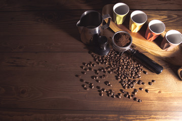 Coffee beans, tamper, portafilter, grinds and espresso cups on a wooden surface.