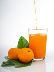 Glass with orange juice and fruits with green leaves