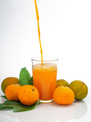 Glass with orange juice and fruits with green leaves