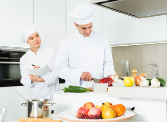 Chefs  in uniform  prepare vegetables with paper recipe on kitchen