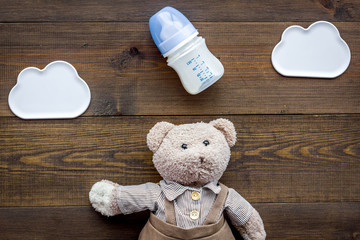 Feed baby concept. Teddy bear toy near small bottle with food on dark wooden background top view space for text