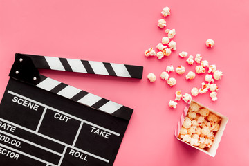 Film watching concept. Clapperboard and popcorn on pink background top view copy space
