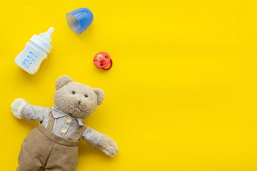 Food for babies concept. Teddy bear toy near small bottle with food on yellow background top view space for text