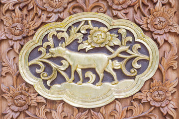 Traditional Thai style wood carving dog of 12 Zodiac,on the wall of temple in Thailand