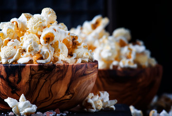 Salted popcorn in a wooden bowl, unhealthy food, dark wooden kitchen table background, selective...
