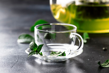 Hot chinese green tea with mint, with splash pouring from the kettle into the cup, steam rises, dark background, selective focus