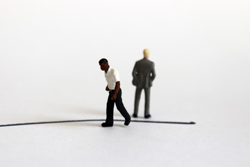 The concept of racial conflict. A miniature black man and a miniature white man standing back from...