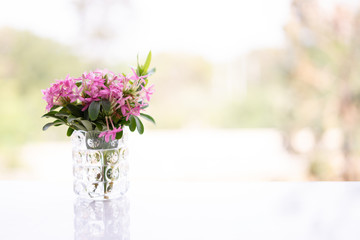 Small beautiful fresh vivid pink flowers in a clear glass vase on the table with copy space and blurred background. Love concept. Decoration concept.