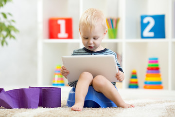 Funny child boy sitting on chamber pot with tablet computer