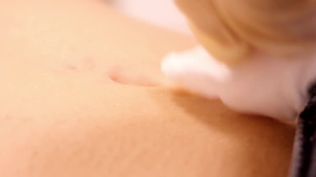 slow motion closeup piercing master in white gloves disinfects skin around client navel with cotton disk