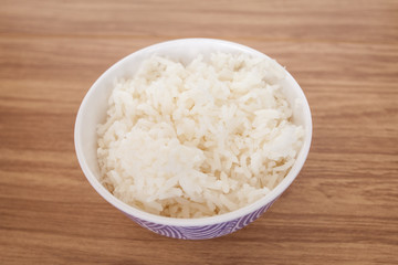 Rice cooked in a white cup placed on a wooden table, ready to serve 