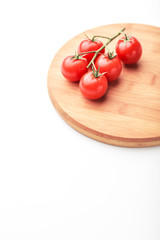 A branch of cherry tomatoes lies on a rectangular cutting board.