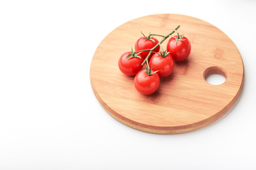 A branch of cherry tomatoes lies on a rectangular cutting board.