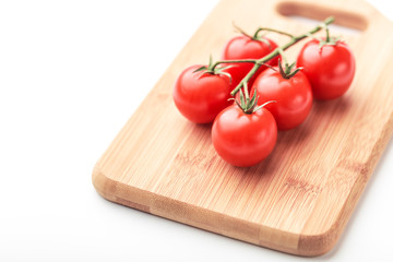 A branch of cherry tomatoes lies on a rectangular cutting board.