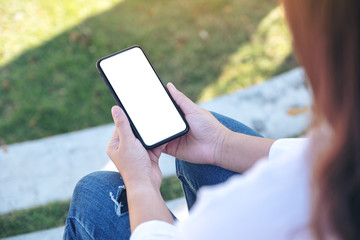 Mockup image of a woman holding black mobile phone with blank white screen while sitting in the outdoors