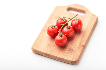 A branch of cherry tomatoes lies on a rectangular cutting board.