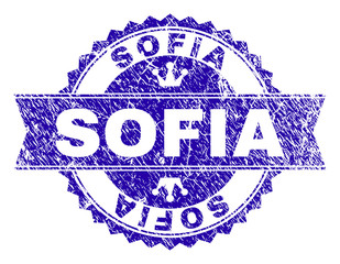 SOFIA rosette seal imitation with grunge style. Designed with round rosette, ribbon and small crowns. Blue vector rubber print of SOFIA label with grunge style.