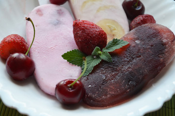 Homemade strawberry cherry banana blueberry ice cream or popsicles decorated green mint leaves on teal rustic table, frozen fruit juice, vintage style, top view