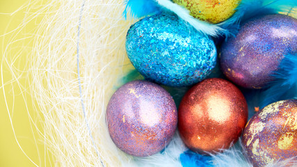 colorful background for easter eggs in a nest with blue feathers. on a yellow background, pastel colors. basket of holiday treats.