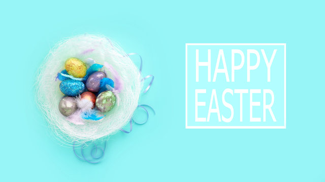 colorful background for easter eggs in a nest with feathers. on a blue background, pastel colors. basket of holiday treats and quote happy easter.