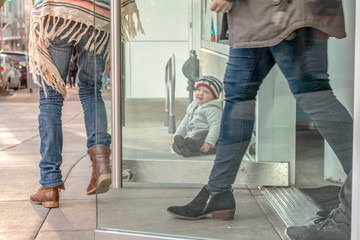 Fototapeta premium A toddler-age boy sits on a city sidewalk outside a bakery