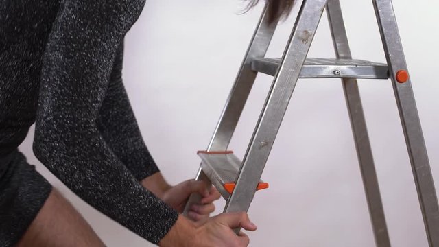 Handsome man in short black shiny gress coming down the stairs. Transgender man with hairy legs in stockings defiantly looking at the camera, smiling