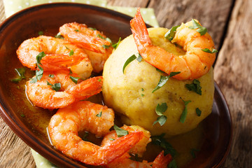 Spicy mofongo with plantains, garlic and chicharron served with shrimp and broth close-up on the table. horizontal