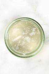 A glass jar with aloe vera gel, shot from the top on a white marble background with a place for text