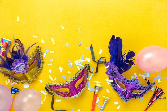 Table top view aerial image of beautiful colorful carnival season or photo booth prop Mardi Gras background.Flat lay variety mask with decorations and confetti & pink balloon on yellow wallpaper.