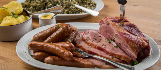 Kassler Nacken, Kohlwurst, Pinkel und Oldenburger Grünkohl auf Platten mit Kartoffeln und Senf auf Holz Tisch