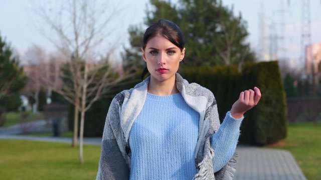 Portrait attractive brunette girl holds banana skin in her hand and throws it on sidewalk then she nods his head negatively in city park on background trees