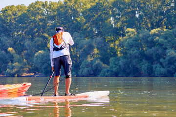 Athletic man paddling on stand up paddle board (paddleboard, SUP) in Danube river at summer