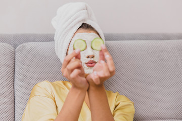 Beautiful young woman doing spa treatments at home, lying with cucumbers in her eyes. Happy and smiling.