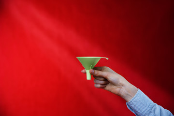 Female hand holding a green funnel on a red background, rays of light. Sifting the truth. Be able to analyze.