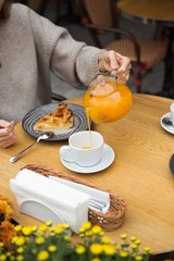 Young attractive smiling woman in gray knitted sweater drinking tea outdoors at the street cafe.