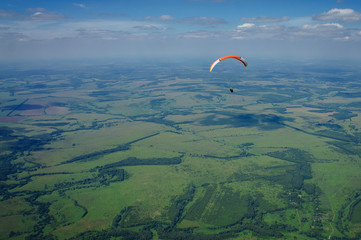 Paraglider flies over green fields. High altitude. The athlete turns the thermal current. Rise up....
