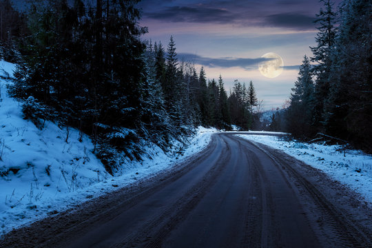 road through pine forest in mountains at night in full moon light. mysterious transportation winter scenery. path winding down the hill
