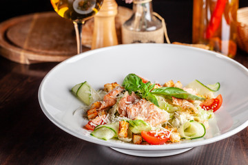 Concept of Italian cuisine. Caesar salad with salmon, lettuce mix, cherry and parmesan cheese. A glass of white wine on the table. Serving dishes in the restaurant. copy space