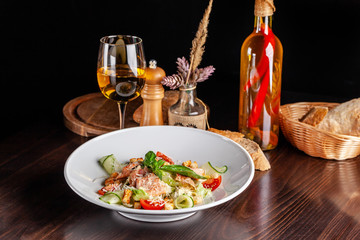 Concept of Italian cuisine. Caesar salad with salmon, lettuce mix, cherry and parmesan cheese. A glass of white wine on the table. Serving dishes in the restaurant. copy space