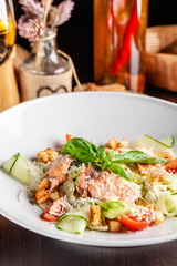 Concept of Italian cuisine. Caesar salad with salmon, lettuce mix, cherry and parmesan cheese. A glass of white wine on the table. Serving dishes in the restaurant. copy space
