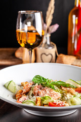 Concept of Italian cuisine. Caesar salad with salmon, lettuce mix, cherry and parmesan cheese. A glass of white wine on the table. Serving dishes in the restaurant. copy space