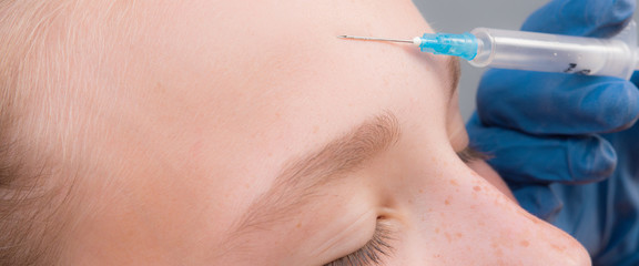 Portrait of a teenage girl doing an injection of botox hyaluronic acid in the skin on the forehead close-up, the concept of youth and beauty