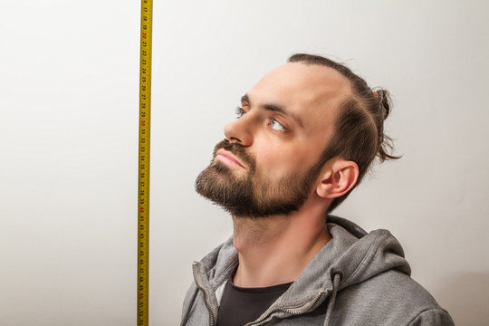 A Man With A Beard Makes Measurements Of His Height With A Tape Measure