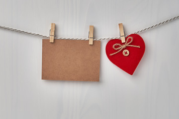 Red heart and blank card hanging on the clothesline on white wooden background