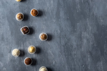 Assortment of fine chocolate candies, white, dark and milk chocolate on grey background. Sweets background, top view.