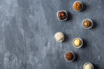 Assortment of fine chocolate candies, white, dark and milk chocolate on grey background. Sweets background, top view, copy space