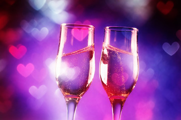 Two glasses of champagne with splash over heart shaped lights