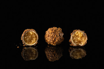 Fine chocolate candy with cheese caramel filling on black background with reflection, close up